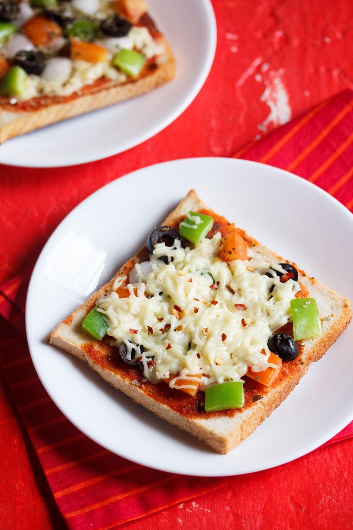 two white serving dishes, each with a slice of bread pizza on a red table with a red cloth underneath.