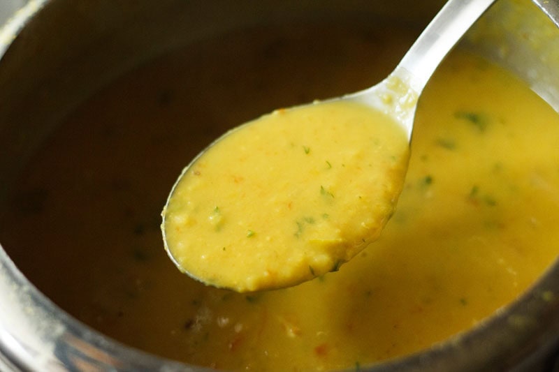 consistency of the lentils or dal being shown with a large spoon.