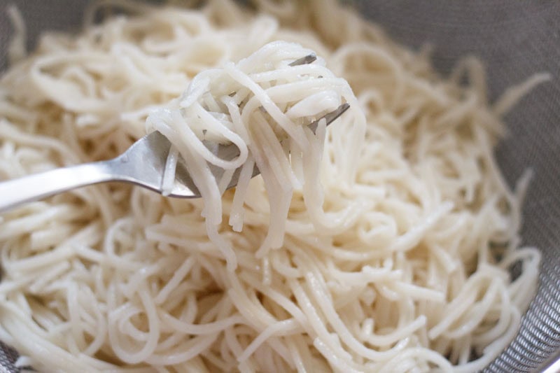 mixing hakka noodles with oil using a fork.