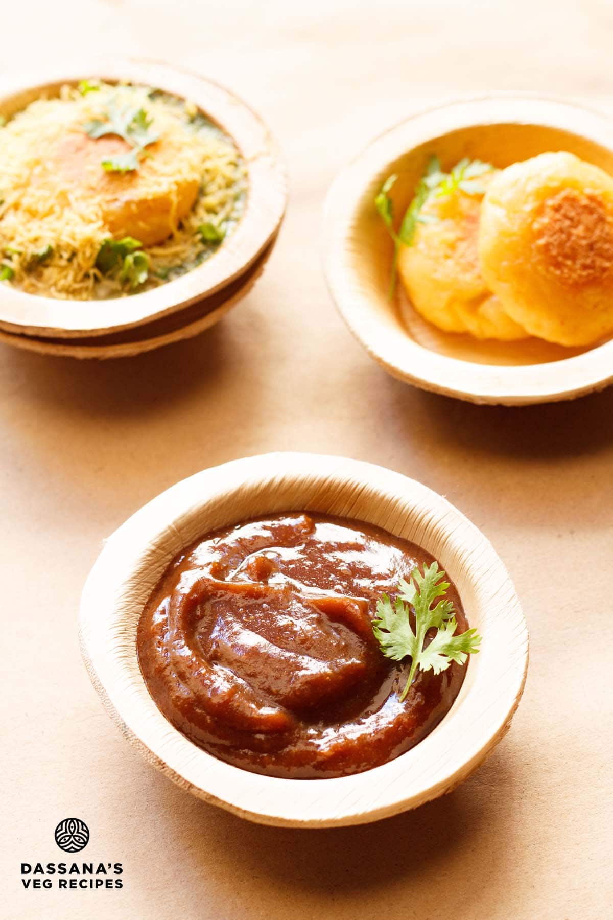 imli chutney garnished with a coriander sprig and served in an Areca leaf bowl on a light brown paper with potato patties and ragda patties chaat in Areca leaf bowls placed on top.