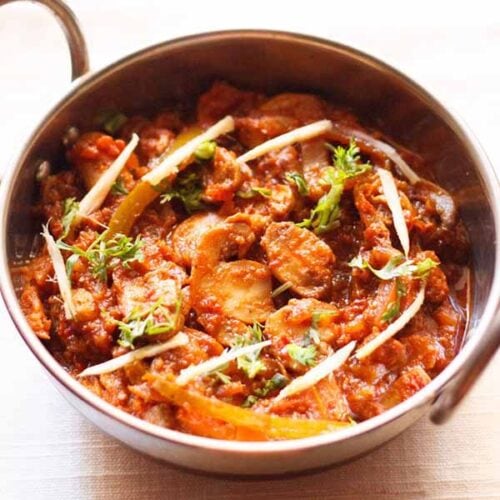 kadai mushroom garnished with coriander leaves, ginger juliennes and served in a steel kadai on a white napkin.