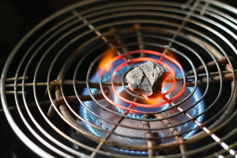 a small piece of charcoal kept on a wired pan and being burnt on a gas-stove flame.