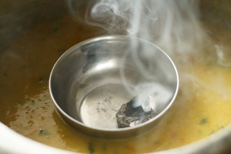 the bowl with the charcoal and the fumes emanating from it has been kept on the dal in the pressure cooker.