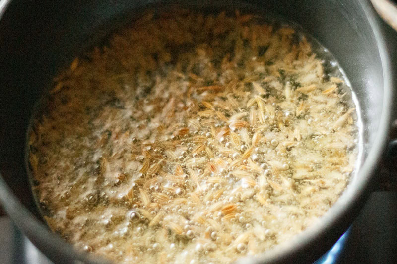 cumin seeds being fried in oil in a small round pan for making tadka for dal.