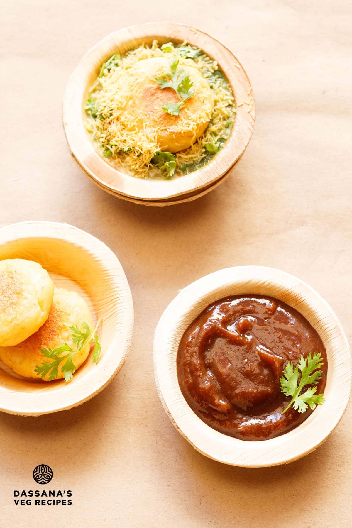 sweet tamarind chutney garnished with a coriander sprig and served in an Areca leaf bowl on a light brown paper with potato patties in areca leaf bowls on left side and ragda patties chaat on top.