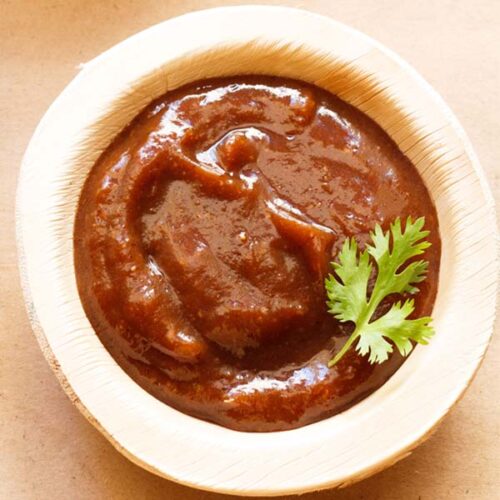 tamarind chutney in a bowl made of areca leaf garnished with a cilantro sprig.